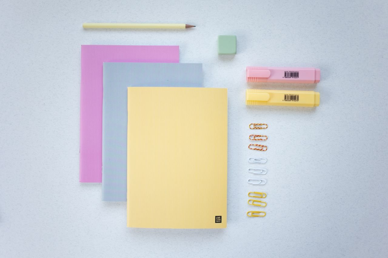 A flat lay of pastel notebooks, highlighters, paper clips, and a pencil, perfect for school or office use.